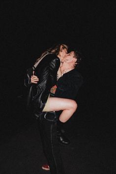 two people are kissing in the dark, one is wearing high heels and the other has a black leather jacket