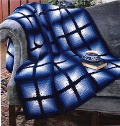 a blue and white blanket sitting on top of a couch next to a cup of coffee