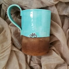 a coffee cup with a bicycle painted on the side sitting on a bed covered in fabric