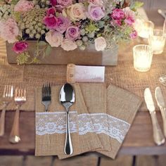 a table set with silverware, napkins and flowers in a vase on top of burlap