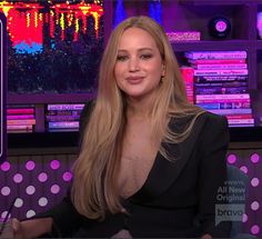 a woman with long blonde hair sitting in front of a tv screen and smiling at the camera