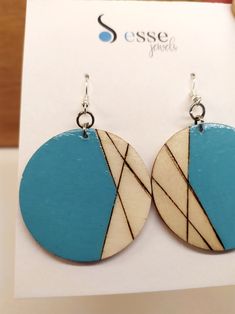 a pair of wooden earrings with blue and white designs on the front, sitting on top of a card