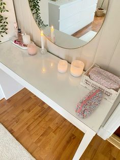 a white vanity with candles on it in front of a large mirror and wooden floor