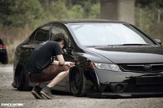 a man kneeling down next to a black car