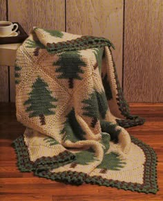 a crocheted blanket is sitting on the floor next to a cup and mug