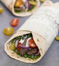 a burrito filled with meat, lettuce and tomatoes on top of a table