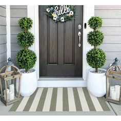 two potted plants are on the front porch next to a door with a monogrammed welcome sign