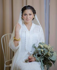 a woman sitting on a chair holding a bouquet and wearing a white veil over her head