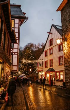 people walking down a cobblestone street at night with christmas lights on the buildings