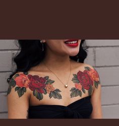 a woman wearing a black dress with flowers on her arm and chest, standing in front of a brick wall