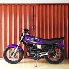 a blue and black motorcycle parked in front of a red metal wall with vertical slats