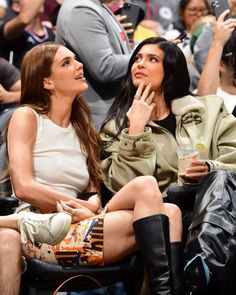 two women sitting next to each other in front of a crowd at a basketball game