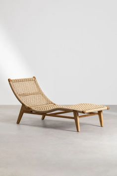 a wooden chaise lounge chair with woven seat padding and back rests against a white wall