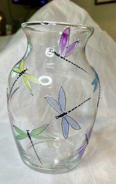 a glass vase with dragonflys painted on the front and sides, sitting on a white tablecloth