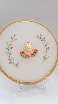 an embroidered object with flowers on it and a gold medal in the center is sitting on a clear stand