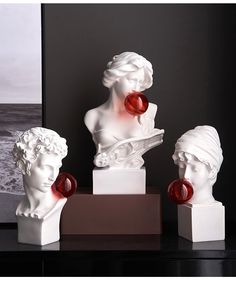 three white busturines with red glass beads on their heads are sitting on a black table