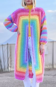 a woman standing in front of a fence wearing a rainbow colored knitted cardigan