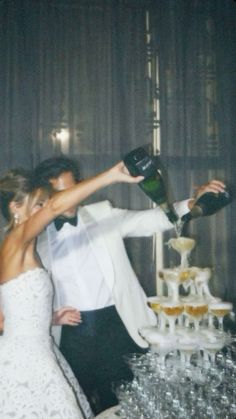 a bride and groom are standing in front of a wedding cake with champagne being poured on it