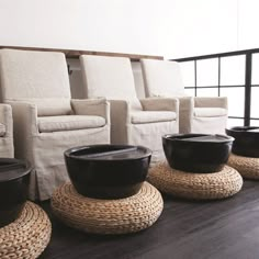 a row of chairs with black bowls on them in front of white couches and windows