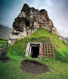 an old building with grass growing on the roof and door in front of a mountain