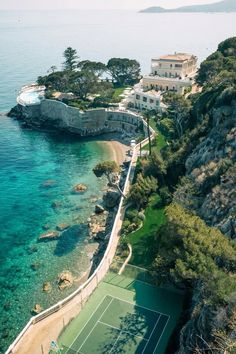 an aerial view of a tennis court near the ocean with houses and cliffs in the background