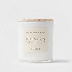 a white candle with the words intention printed on it and a wooden lid sitting in front of a white background