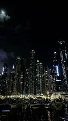 the city skyline is lit up at night with boats in the water and full moon