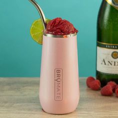 a pink cocktail with raspberries in it next to a bottle of champagne