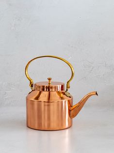 a copper tea pot with a gold handle on a white surface, against a plain background