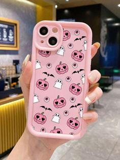 a woman holding up a pink phone case with pumpkins and ghost faces on it