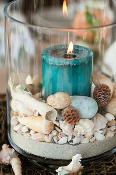 a candle that is sitting on some rocks and sand in a glass container with shells around it