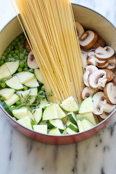 a pot filled with pasta and vegetables on top of a counter next to chopsticks