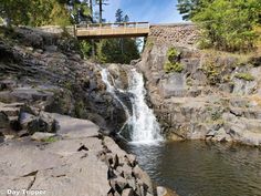 a waterfall with a bridge over it next to some rocks