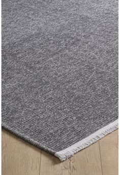 a grey rug with fringes on the bottom and wood flooring in front of it