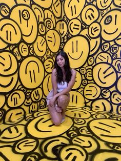 a woman sitting on the ground in front of a yellow and black wall with circles