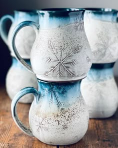 three blue and white mugs with snowflakes on them sitting on a wooden table