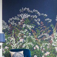 a blue chair sitting in front of a wall with flowers on it and a lamp next to it