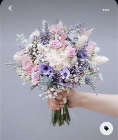 a bouquet of flowers being held by someone's hand in front of a gray wall