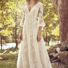 a woman in a white wedding dress is standing near some trees and rocks with her hands on her hips