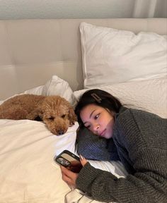 a woman laying in bed next to a dog holding a cell phone