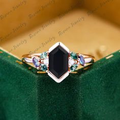 a ring with an oval cut black diamond surrounded by multi - colored stones on a green velvet box