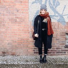 a woman standing in front of a brick wall with a scarf around her neck and boots on