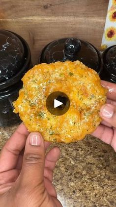 a person holding up a doughnut in front of some black containers with food on them