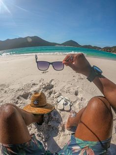 a person laying on the beach with their feet up in the sand while wearing sunglasses and a hat