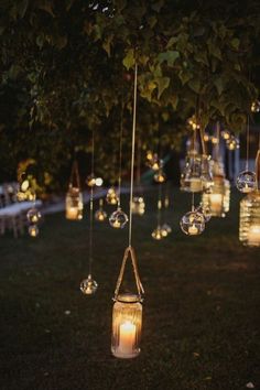 some lights hanging from a tree in the dark with candles on them and glass jars filled with water