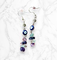 These Evil Eye + Fluorite Earrings are crafted with natural fluorite crystals and finished off with sterling silver hooks, making them a stylish and unique piece of jewelry. Handmade with expert care, these earrings are sure to be a favorite in any collection! Properties of fluorite: - Increases intuition - Protection from negative energies - Purifies and calms the atmosphere around you - Increases focus and assists in decision-making Each pair includes: - 2 high-quality sterling silver earring hooks - 8 natural fluorite chips - 2 durable metal evil eye charms - 2 silicone earring backs Earring drop length: 2 in. Evil Eye Handmade Jewelry, Spiritual Crystal Earrings As Gift, Handmade Crystal Drop Earrings For Healing, Nickel-free Amethyst Earrings For Healing, Spiritual Crystal Earrings With Natural Stones For Gift, Healing Amethyst Earrings With Natural Stones, Hypoallergenic Spiritual Dangle Earrings, Spiritual Dangle Plug Earrings As Gift, Handmade Mystical Crystal Earrings As Gift