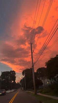 the sun is setting behind some power lines and telephone poles in this photo, cars are parked on the side of the road