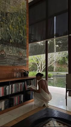 a woman sitting on the floor reading a book in front of a bookshelf