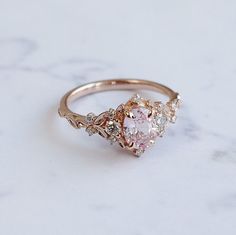 a pink diamond ring sitting on top of a white marble countertop next to a pair of scissors