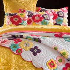 a bed with yellow and pink bedspread, pillows and flowers on the comforter